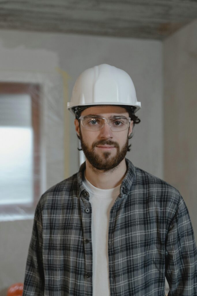 pexels-photo-6474475-6474475 Portrait of a construction worker wearing a hard hat and safety glasses inside a building.